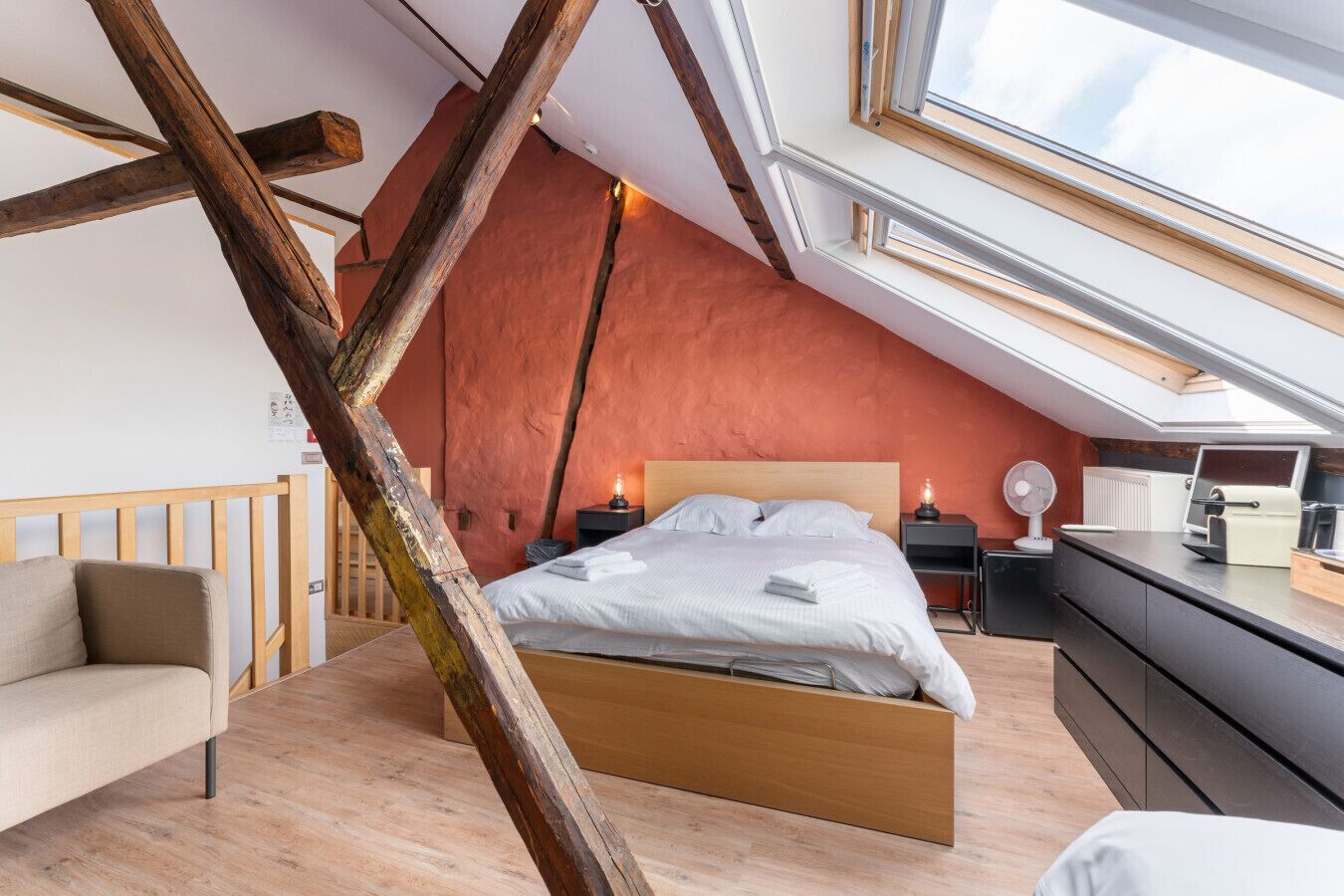 Une chambre avec un plafond en pente, un lit, des tables de chevet, un bureau et une chaise.