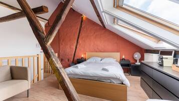 Une chambre avec un plafond en pente, un lit, des tables de chevet, un bureau et une chaise.