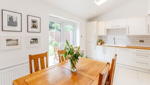 Una cocina moderna con armarios blancos, una mesa de comedor de madera y cuadros en la pared.