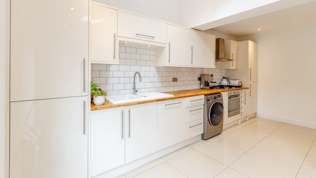 Una cocina moderna con armarios blancos, encimera de madera, lavadora integrada y salpicadero de azulejos.