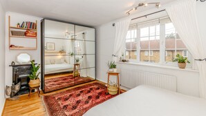Un dormitorio con cama, espejo, estantería, ventana con cortinas y radiador.