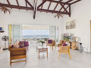 A spacious living area with a balcony, wooden furniture, a TV, and a fan. - Single-storey house with pool & sea view, sleeps 6 (Sainte-Luce)