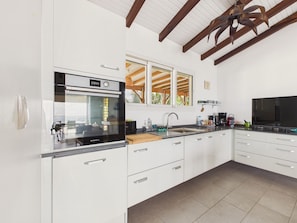 A modern kitchen with white cabinetry, a built-in oven, a sink, and a large window. - Single-storey house with pool & sea view, sleeps 6 (Sainte-Luce)