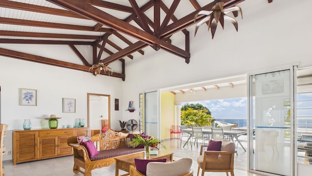 Amplia sala de estar con techo de madera, un comedor y vista al mar a través de amplios ventanales.