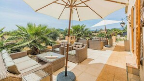 An outdoor patio with wicker furniture, a large umbrella, and a view of the surrounding landscape. - Modern design Mallorca estate among nature (Búger)