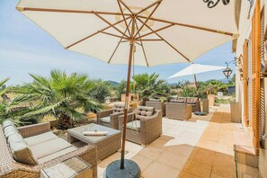 An outdoor patio with wicker furniture, a large umbrella, and a view of the surrounding landscape. - Modern design Mallorca estate among nature (Búger)