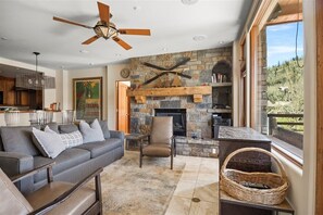 A living room with a stone fireplace, a ceiling fan, and a view of the outdoors. - Mountain Village Gem | Ski-In/Out + Steam Shower (Mountain Village)
