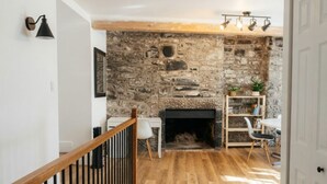 Una habitación con pared de piedra, chimenea, suelo de madera, un escritorio blanco y una silla blanca.