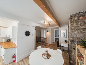 A modern kitchen with wooden countertops, a dining area with a round table, and a stone wall. - 2 Renovated Bedrooms | Historic + Modern Charm in the Heart of Old Quebec (Québec)