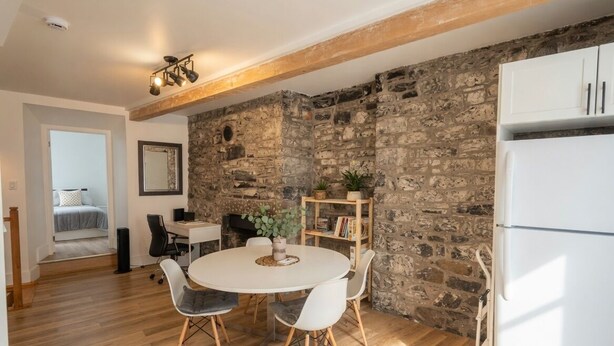 Una habitación con pared de piedra, una mesa de comedor blanca con sillas, un refrigerador blanco y suelo de madera.