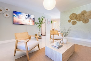 Una sala de estar moderna con dos sillas de madera, una mesa de centro, un televisor y decoración en la pared.