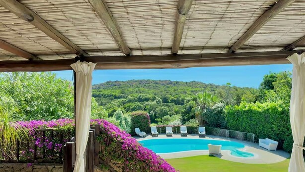 A covered outdoor area with a pool, lounge chairs, and a view of a mountainous landscape. - Villa Iole by My Villa Collection (Cala di Volpe)