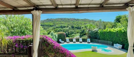A covered outdoor area with a pool, lounge chairs, and a view of a mountainous landscape.
