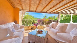A covered outdoor seating area with white furniture and a view of greenery. - Villa Iole by My Villa Collection (Cala di Volpe)