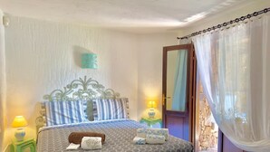A bedroom with a bed, two bedside tables, a nightstand, a door, and a curtain. - Villa Iole by My Villa Collection (Cala di Volpe)