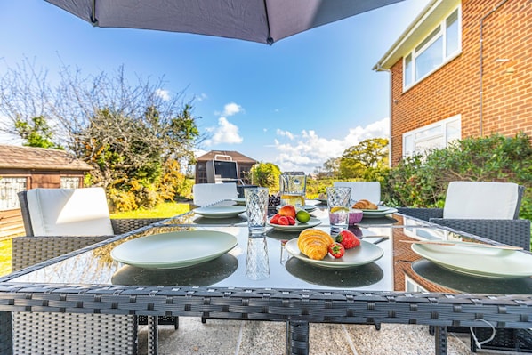 An outdoor dining area with a table set for breakfast, surrounded by wicker chairs and an umbrella.