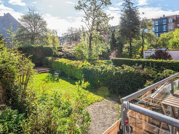 Un jardin luxuriant avec une terrasse en bois, des haies touffues et une grande variété d’arbres.