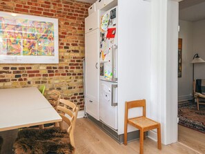 A room with a brick wall, a white refrigerator with children's drawings, a wooden table, and chairs.