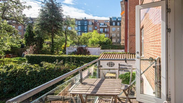 A balcony with a wooden table and chairs, a metal railing, and a view of a brick building and greenery. - 3 Person Holiday Home in Aarhus C (Aarhus)