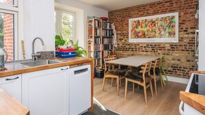 A kitchen with a brick wall, wooden cabinets, a dining table with chairs, and a bookshelf. - 3 Person Holiday Home in Aarhus C (Aarhus)