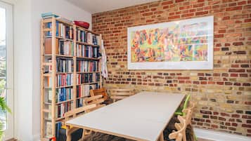 A room with a brick wall, a bookshelf, a framed abstract painting, a table, and a chair with a fur throw.