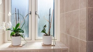 A bathroom with two potted plants on a ledge, a window with frosted glass, and tiled walls. - 3 Person Holiday Home in Aarhus C (Aarhus)