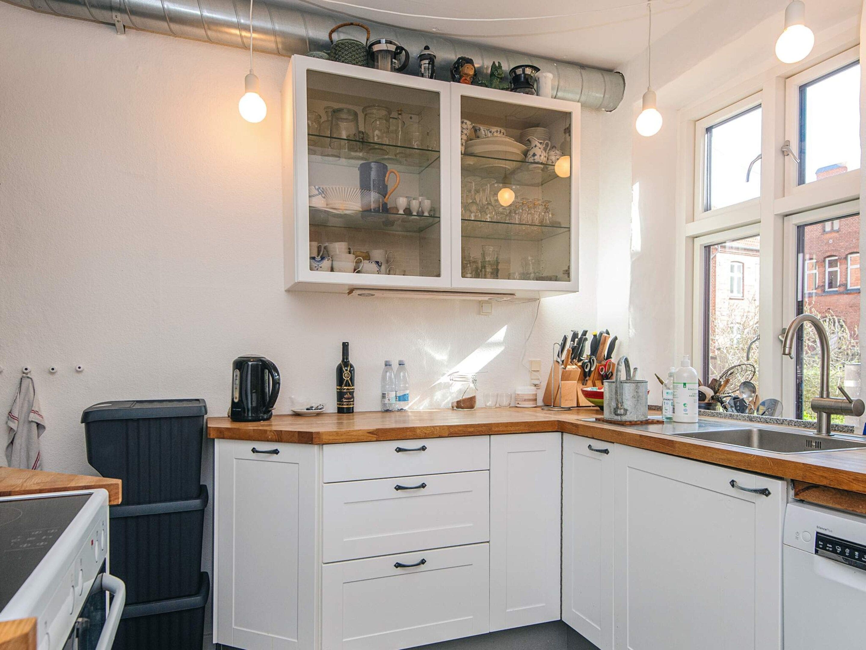 Een keuken met witte kastjes, een ingebouwde oven, een koffiezetapparaat en een raam met uitzicht op een gebouw.