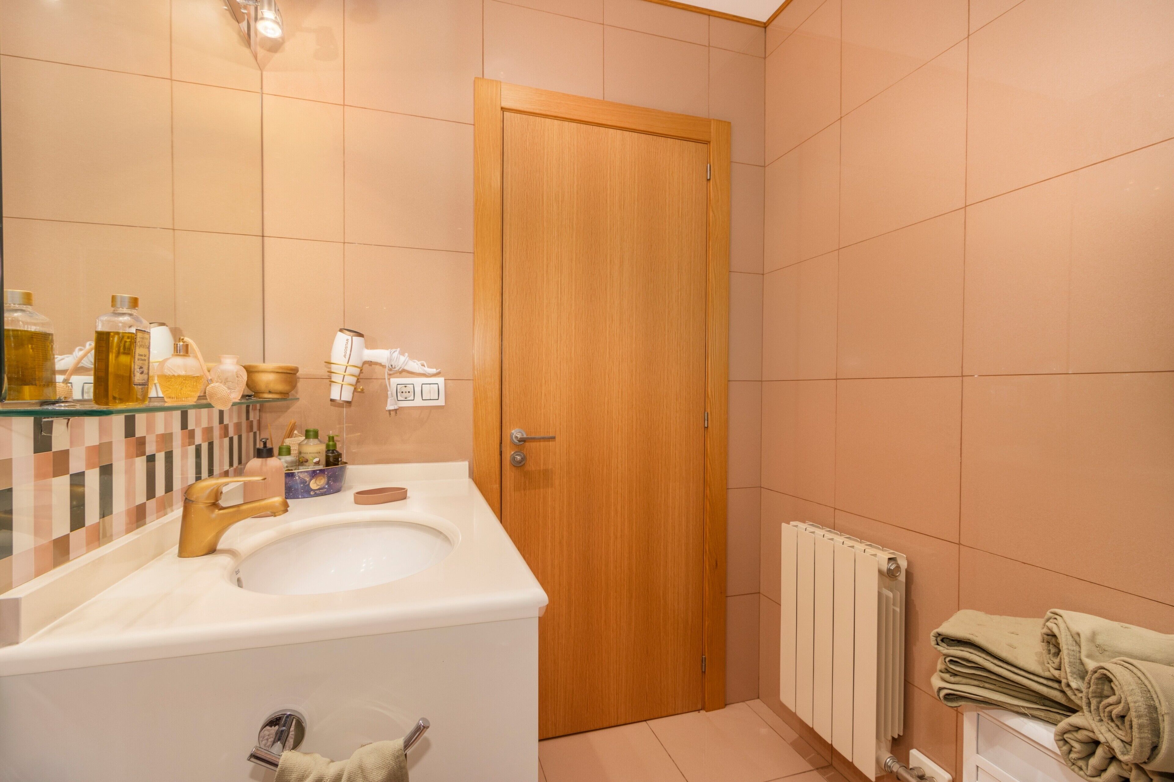 Un baño con lavamanos, artículos de aseo, toallero y una puerta de madera.