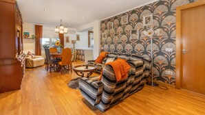Ein Wohnzimmer mit einer Couch, einem Esstisch und Stühlen, einer Küchenzeile und einer Wand mit Muster.