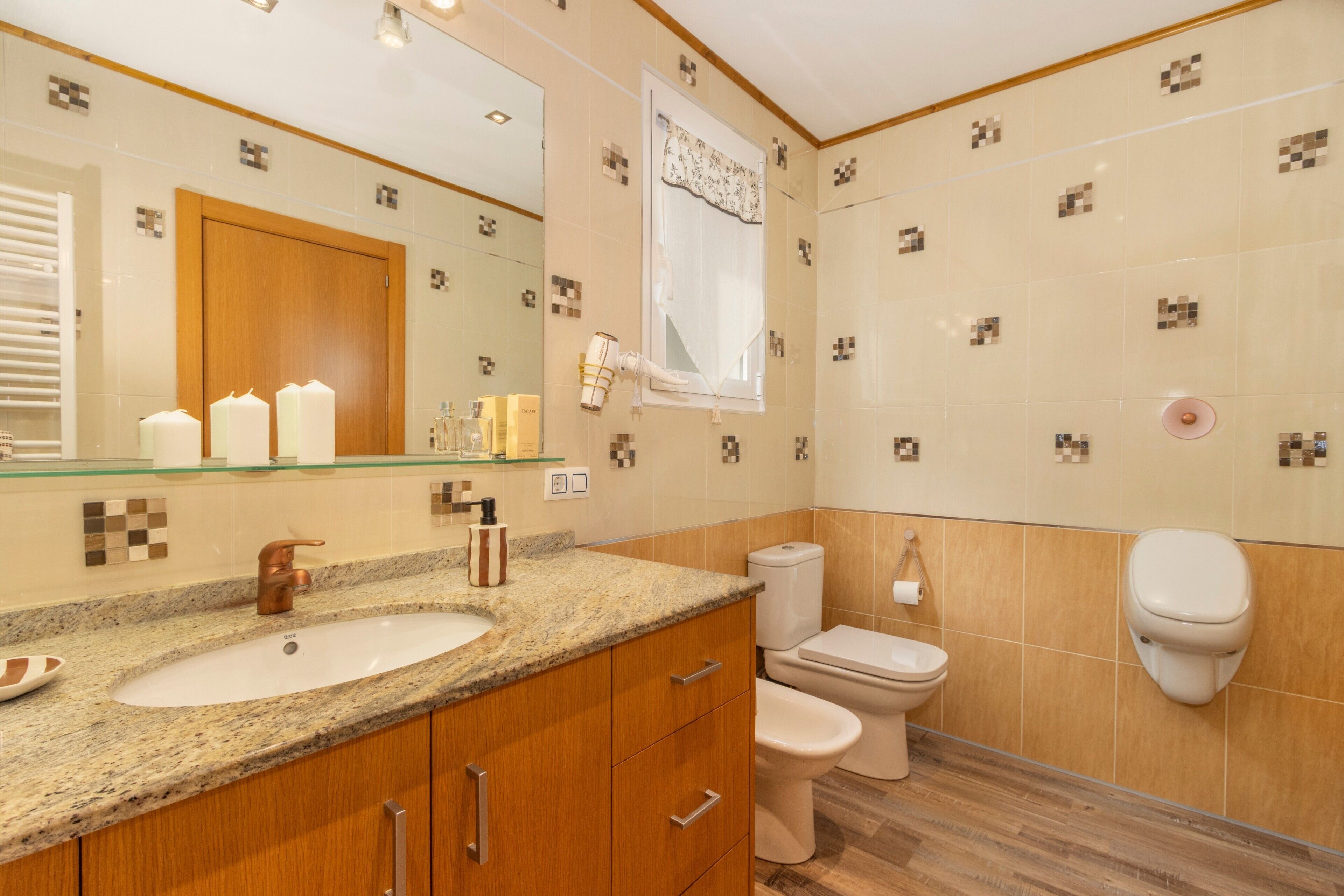 Un baño con encimera de granito, armarios de madera, un lavabo blanco, inodoro y espejo.