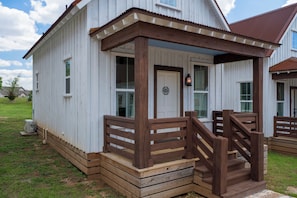 Un bâtiment en bois peint en blanc, doté d’un porche, d’un escalier en bois et d’une porte sur laquelle est apposée une enseigne.
