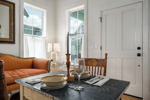 Un coin repas avec une table dressée pour deux personnes, une chaise en bois, un canapé rembourré et une fenêtre avec des rideaux.