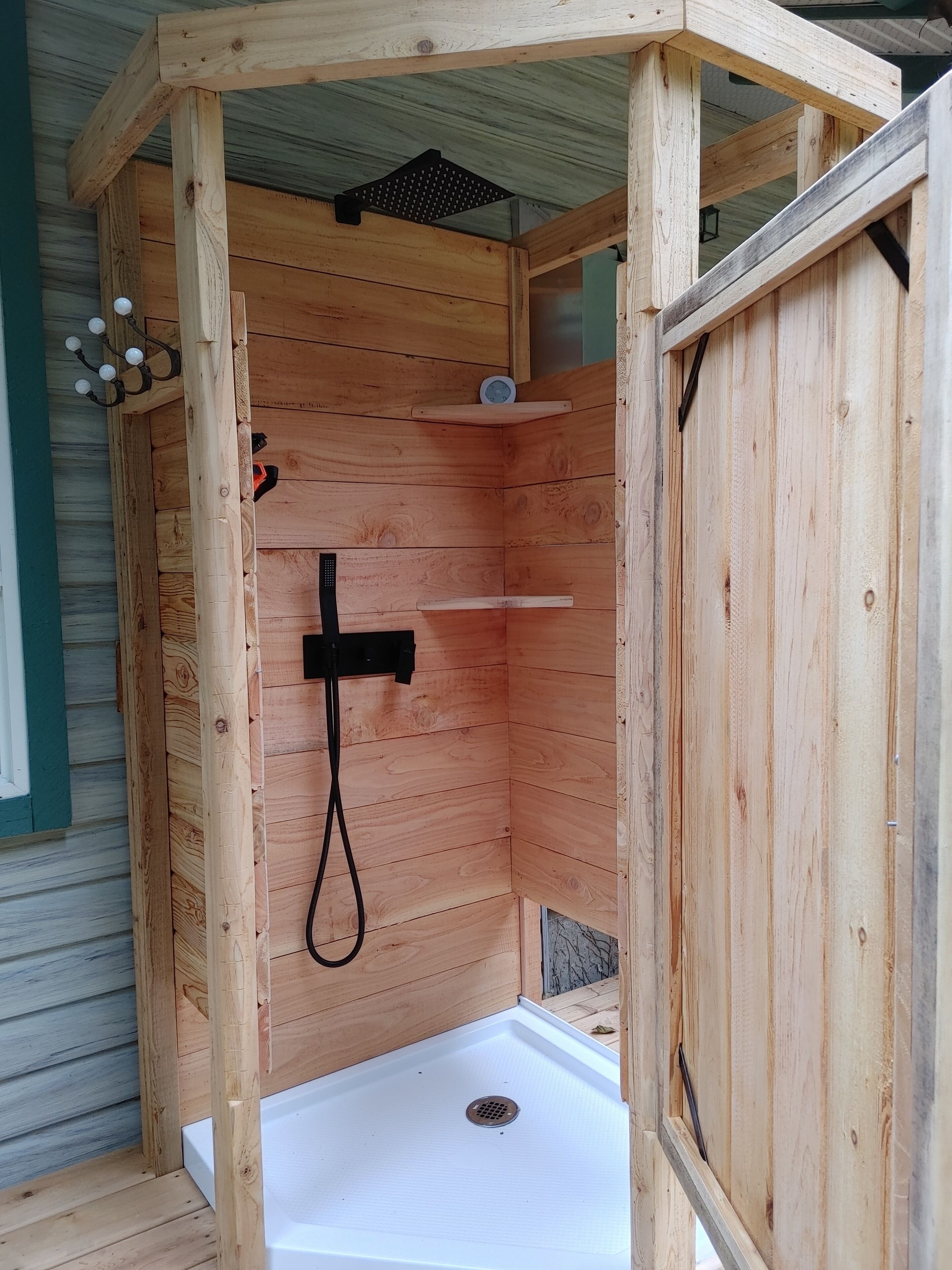 Cabina de ducha de madera con suelo blanco, un cabezal de ducha de mano y un estante pequeño.