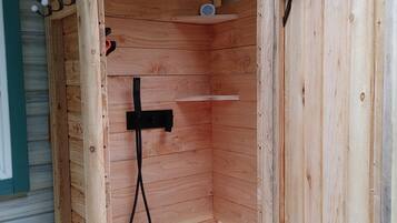Cabina de ducha de madera con suelo blanco, un cabezal de ducha de mano y un estante pequeño.