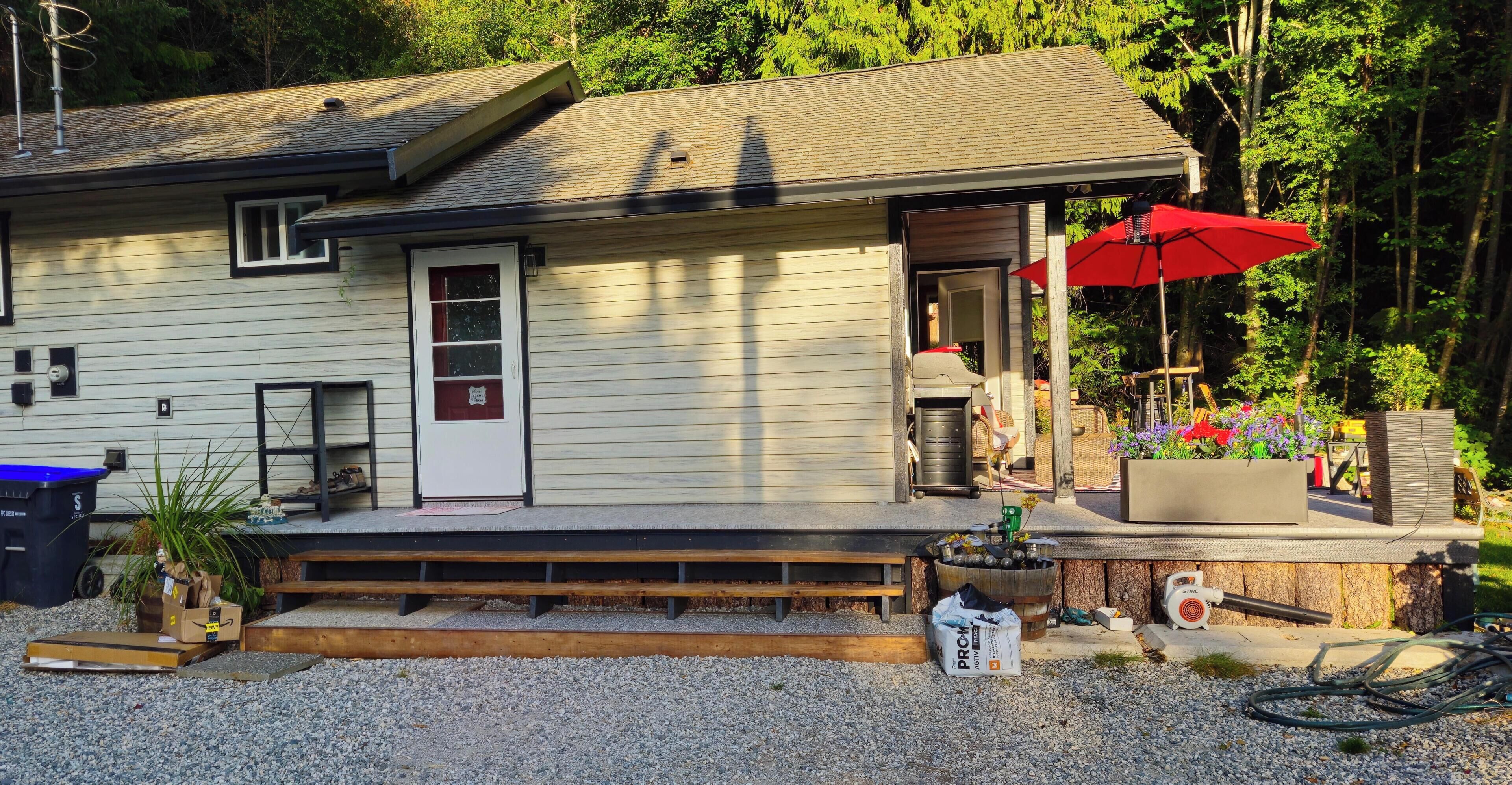 A single-story house with a porch, a red umbrella, and a garden area with plants and flowers.