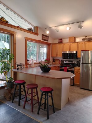 Une cuisine moderne avec des meubles en bois, un réfrigérateur en acier inoxydable, un four encastré et un grand îlot central doté de tabourets.