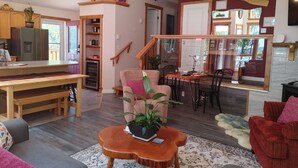 Een gezellige woonkamer met een houten eettafel, een bank, een rode fauteuil en een klein houten salontafel met een plant.