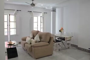 A living room with a sofa, a dining table, and a ceiling fan. - Elegant apartment in Sierpes by Panther Home (Sevilla)