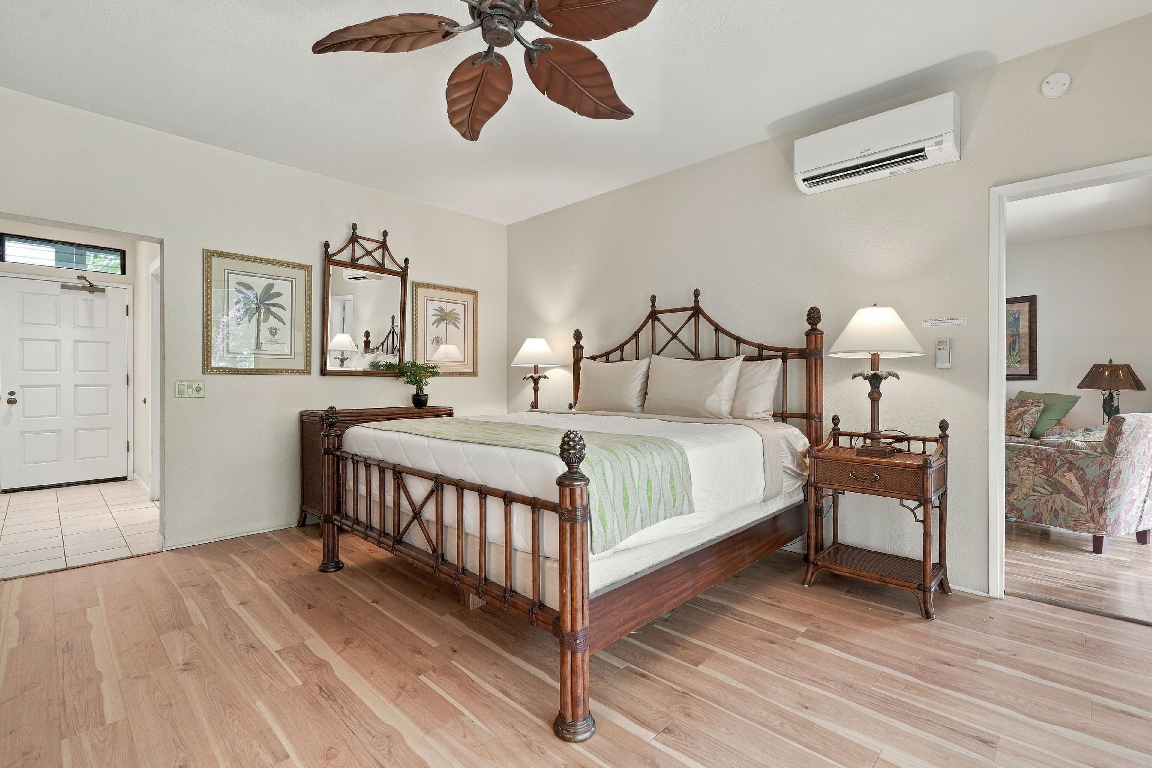 Quarto com cama de madeira, ventoinha no teto, mesa de cabeceira, abajur e porta.