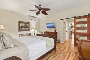A bedroom with a bed, a ceiling fan, a mounted TV, and a wooden dresser. - Wailea Blue Golf Course Condo-Walk to Shops (Kihei)