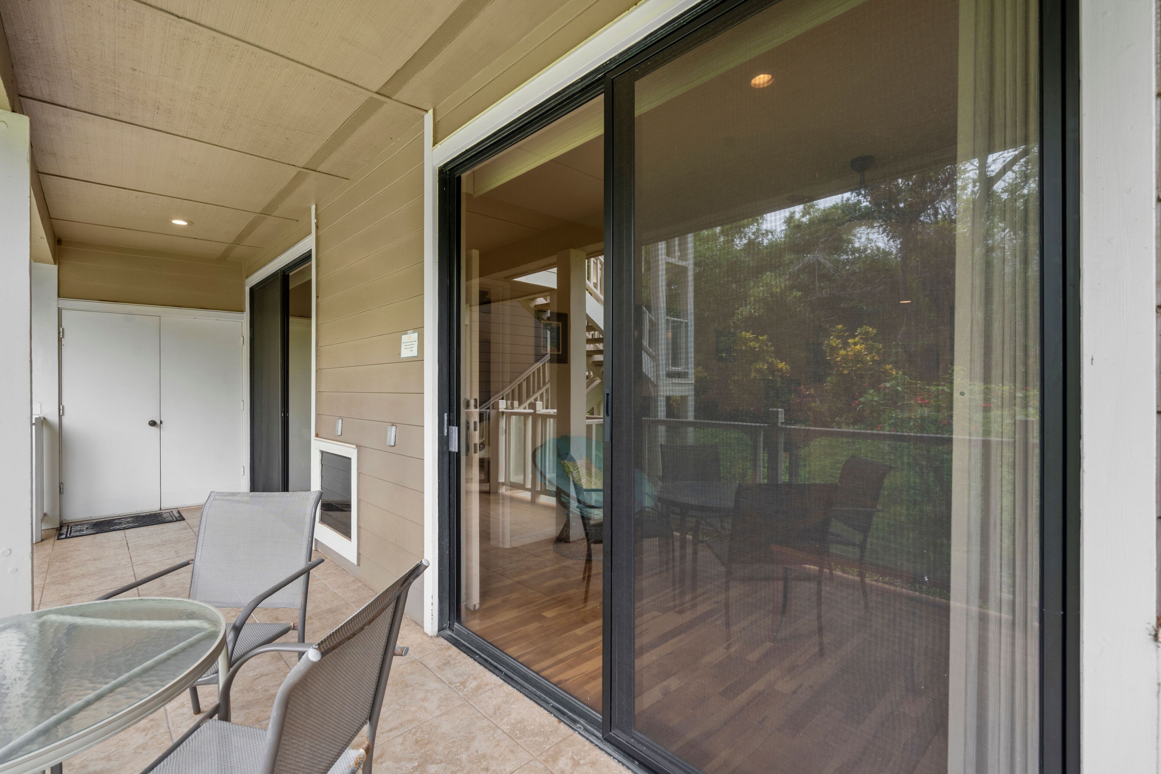 Un espace extérieur abrité, doté d’une porte vitrée donnant sur une terrasse en bois, une table en verre et deux chaises.