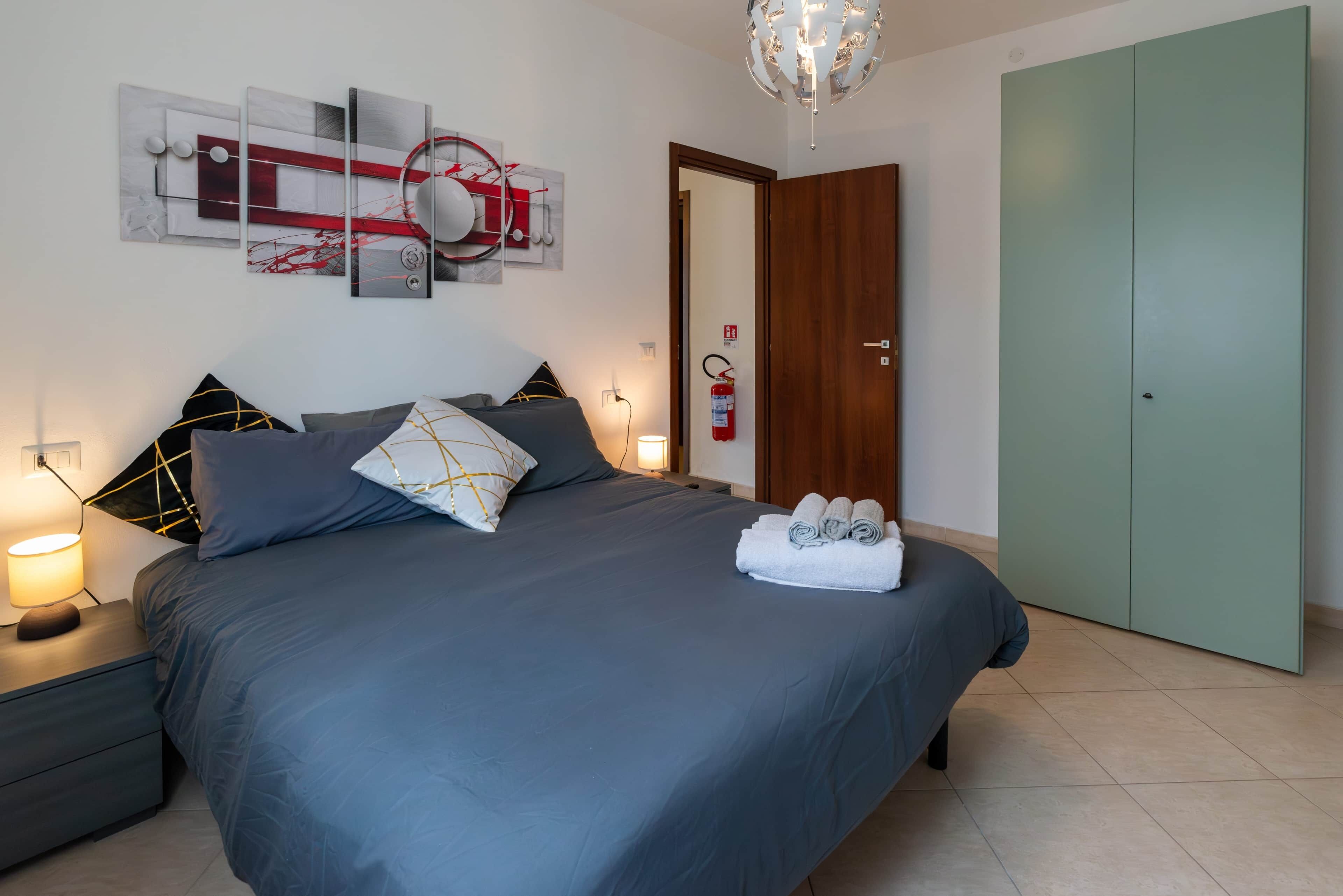 Ein Schlafzimmer mit Bett, Nachttischen, einem Wandbild, einer Tür und einem Kleiderschrank.