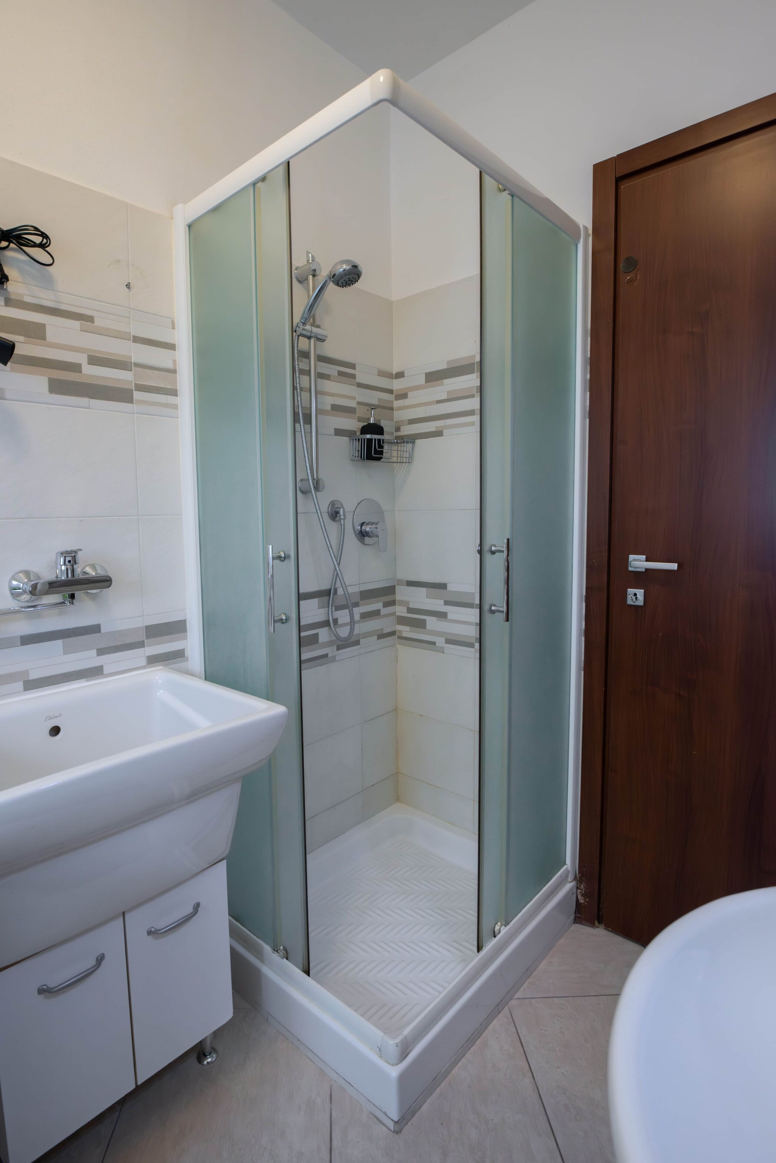 Een moderne badkamer met een douchecabine van glas, een witte wastafel en een houten deur.