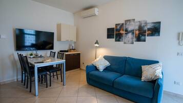 Una sala de estar moderna con un televisor de pantalla plana, una mesa de comedor con sillas, un sofá azul y arte abstracto en la pared.