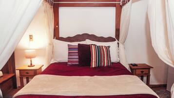 A bed with a red bedspread, multiple pillows, a wooden headboard, and a bedside table with a lamp.