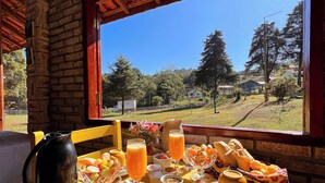 Mesa de café da manhã com diversos alimentos e vista para uma paisagem rural.