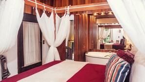 Um quarto com cama, cortinas, teto de madeira, janela e banheiro.