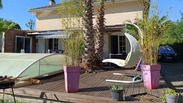 Ein Haus mit einer Holzterrasse, einem Pool und einem Auto auf der Auffahrt.