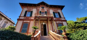 Un bâtiment historique doté d’une entrée imposante, d’un balcon et d’un escalier menant à la porte.