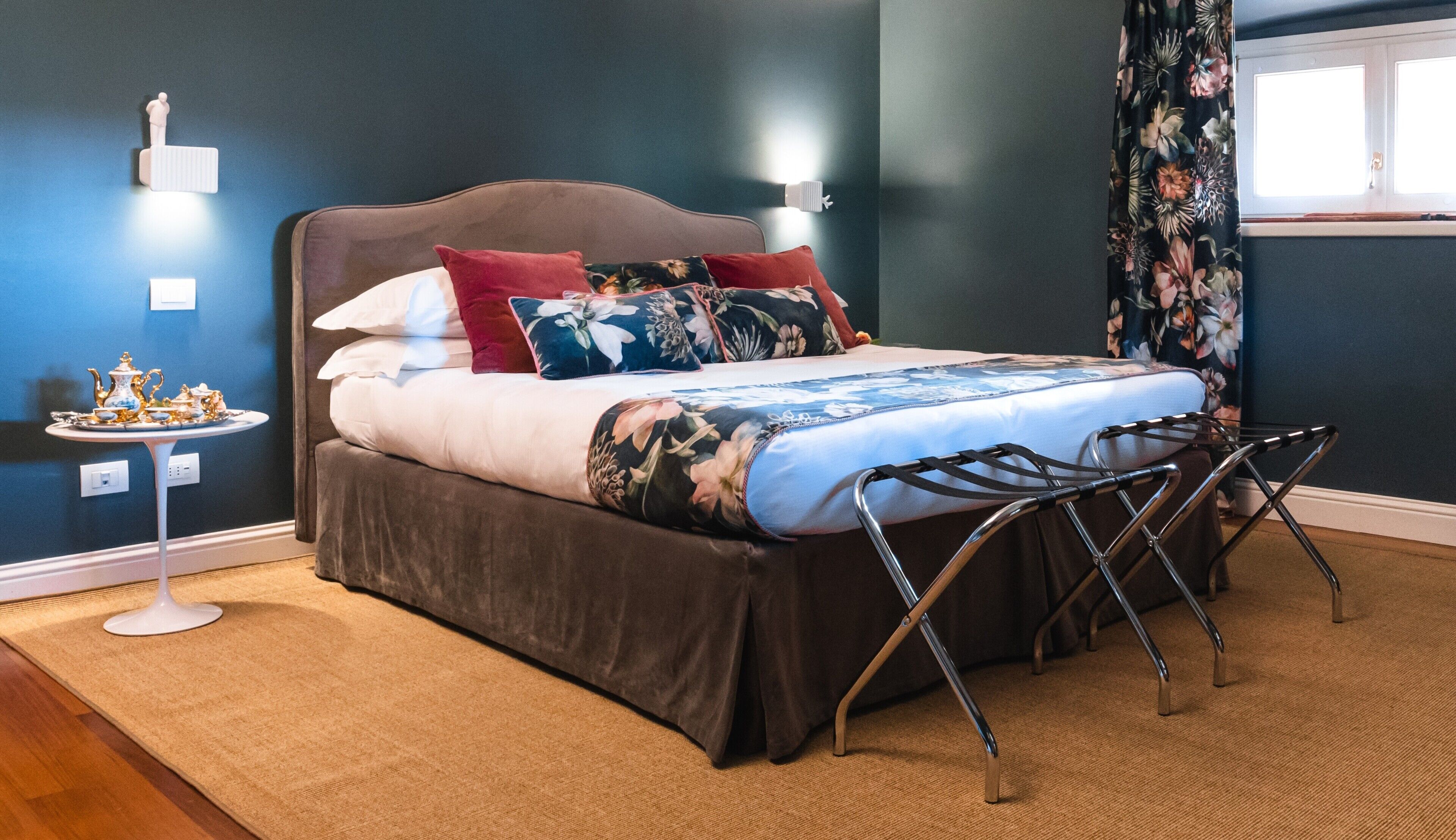 Un letto con una coperta a fiori, un tavolino con una teiera e un comodino con una lampada.